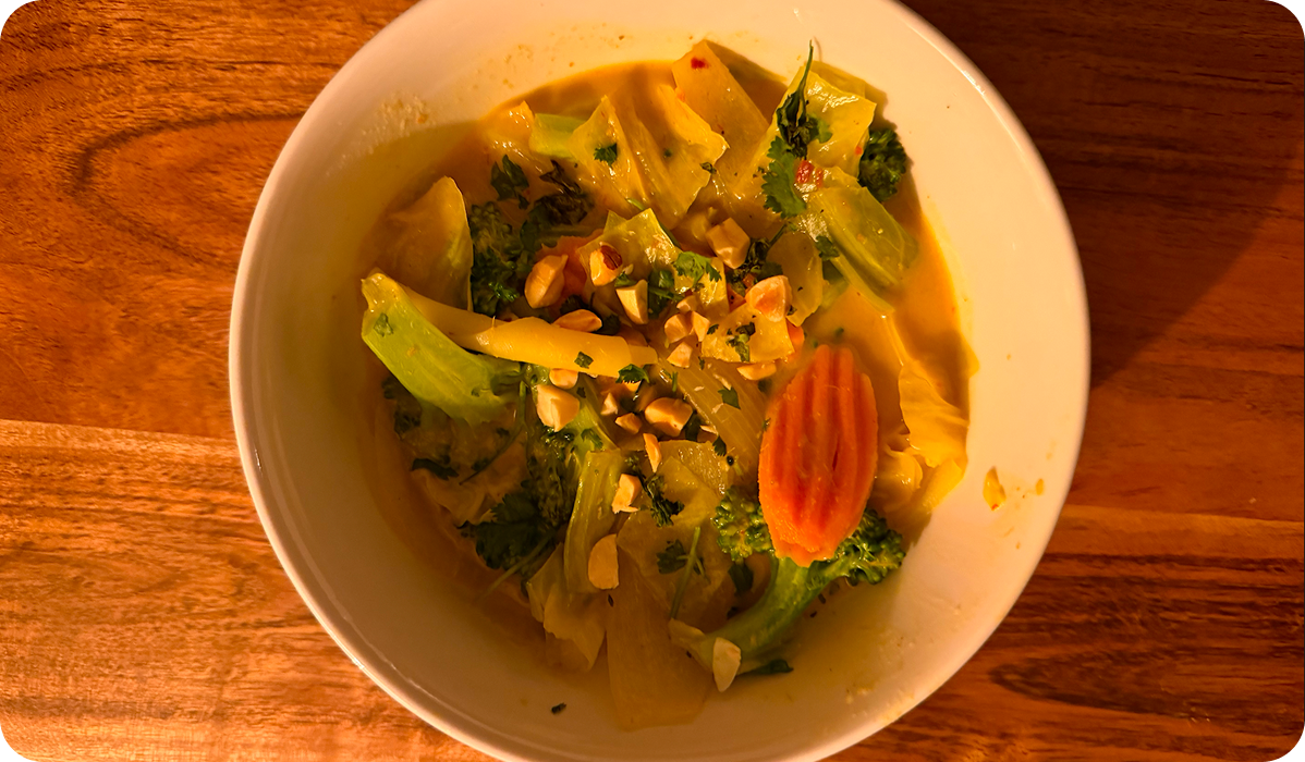 A bowl of vegetable curry with broccoli, cabbage, carrots, and crushed peanuts on a wooden table